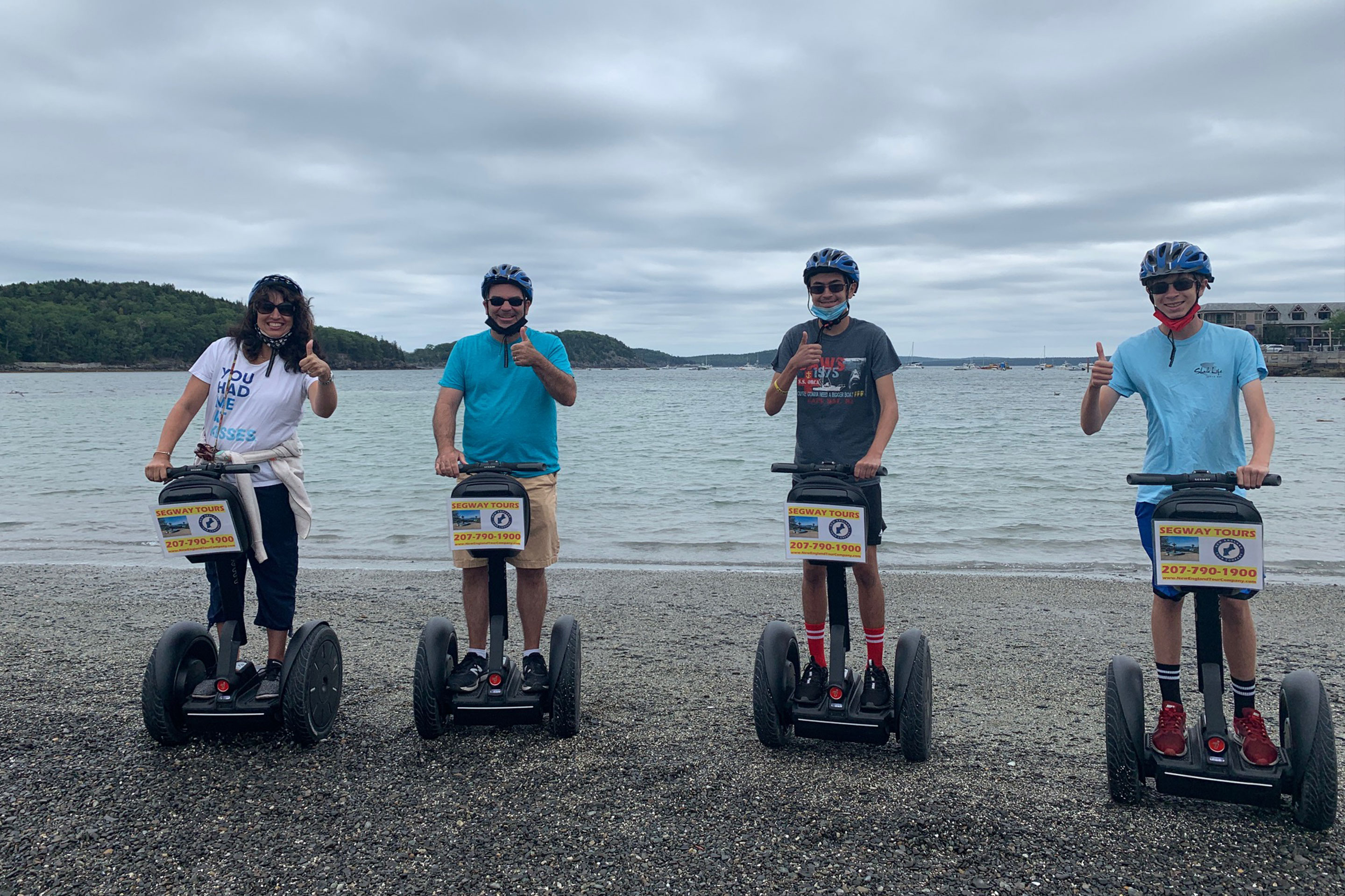 Jennifer (left) and her family stand on Segway's wearing helmets and masks for their safety along the edge of the waterfront.