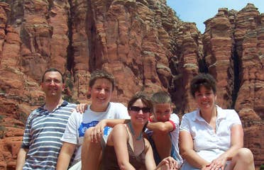 A caucasian family sits facing the camera in front of Sedona Red rocks.