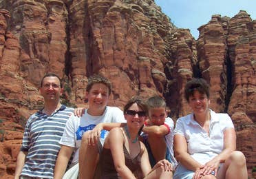 A caucasian family sits facing the camera in front of Sedona Red rocks.