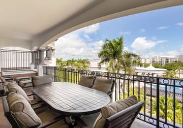 Balcony dining area with lounge chairs and lush resort scenery.