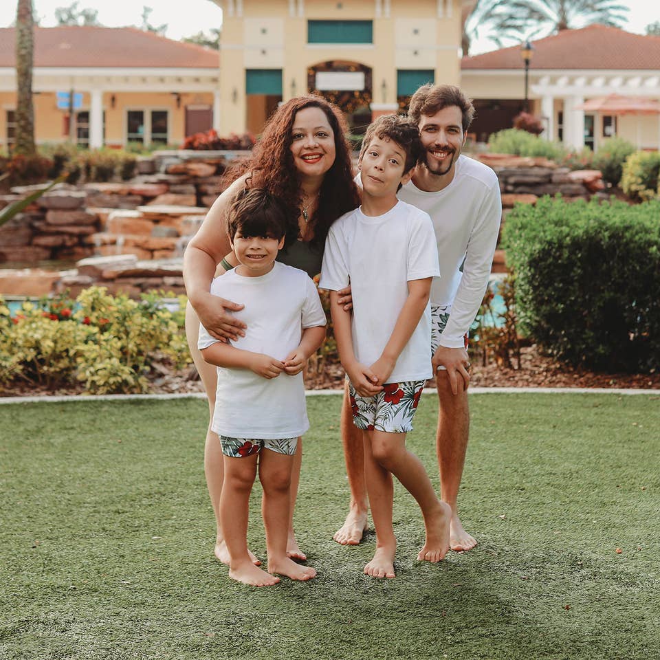 A woman, man and two young boys wear swimwear while standing near a building and lazy river.