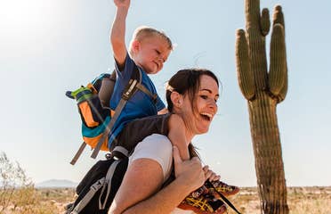 Jessica and her son laughing together while he sits on her shoulders as they hike in the Arizona desert.