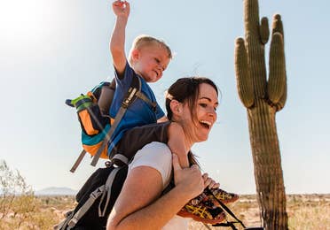 Jessica and her son laughing together while he sits on her shoulders as they hike in the Arizona desert.