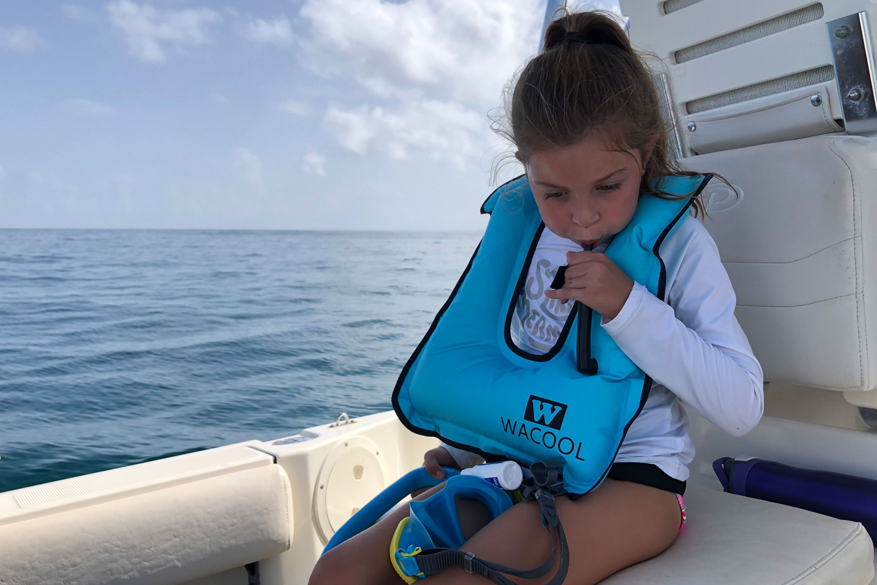 Featured Contributor, Chris Johnston's daughter, Kyler inflates her Wacool snorkel vest while sitting on a boat in the ocean.
