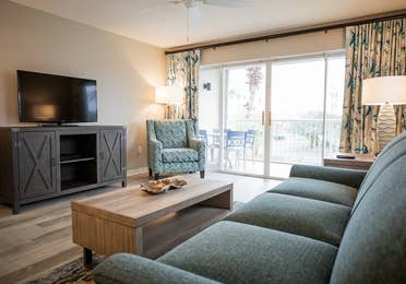 Living room with couch, chair, flat screen TV and balcony in a villa at Cape Canaveral Beach Resort.