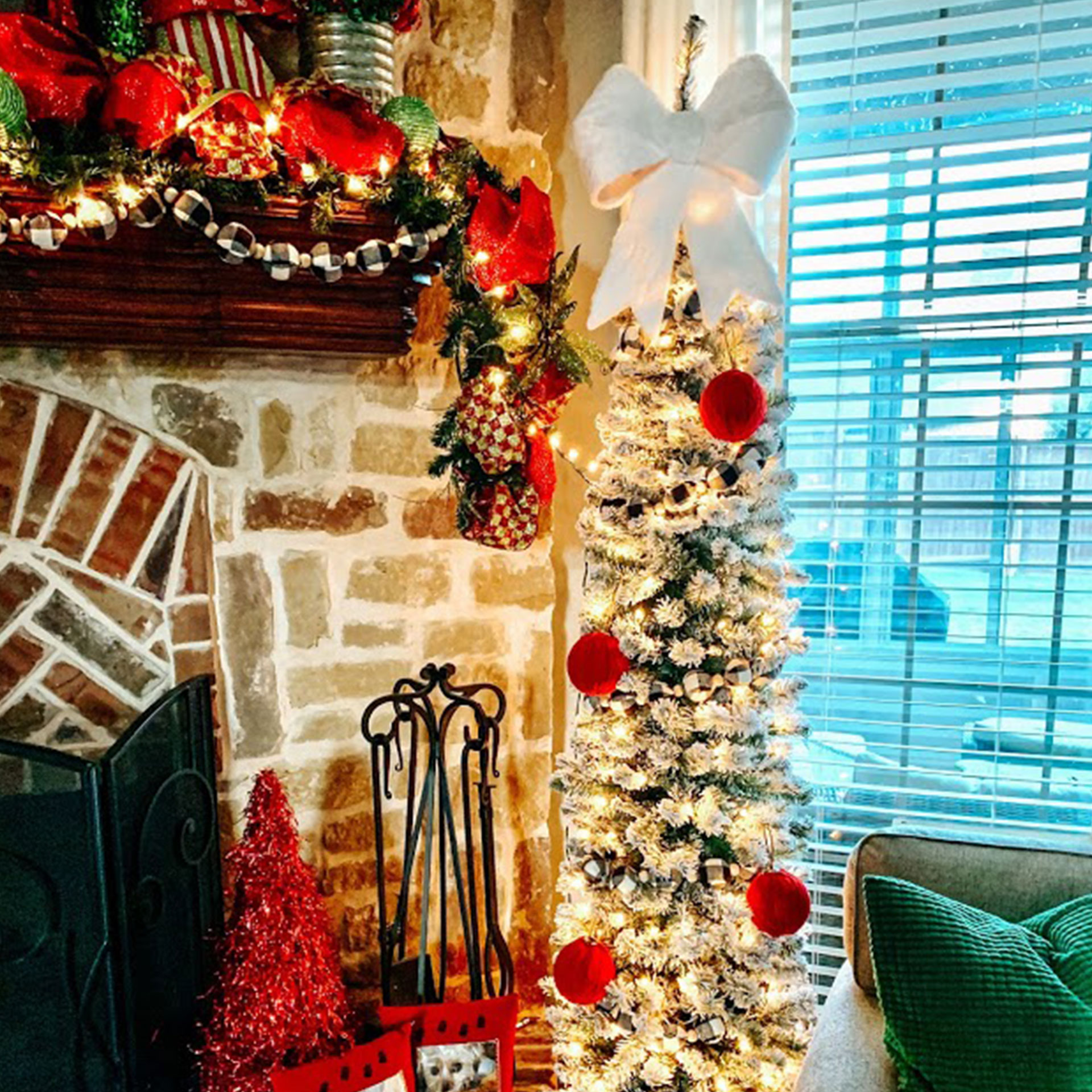 A small 'pencil tree' decked out in holiday decor next to a mantle.