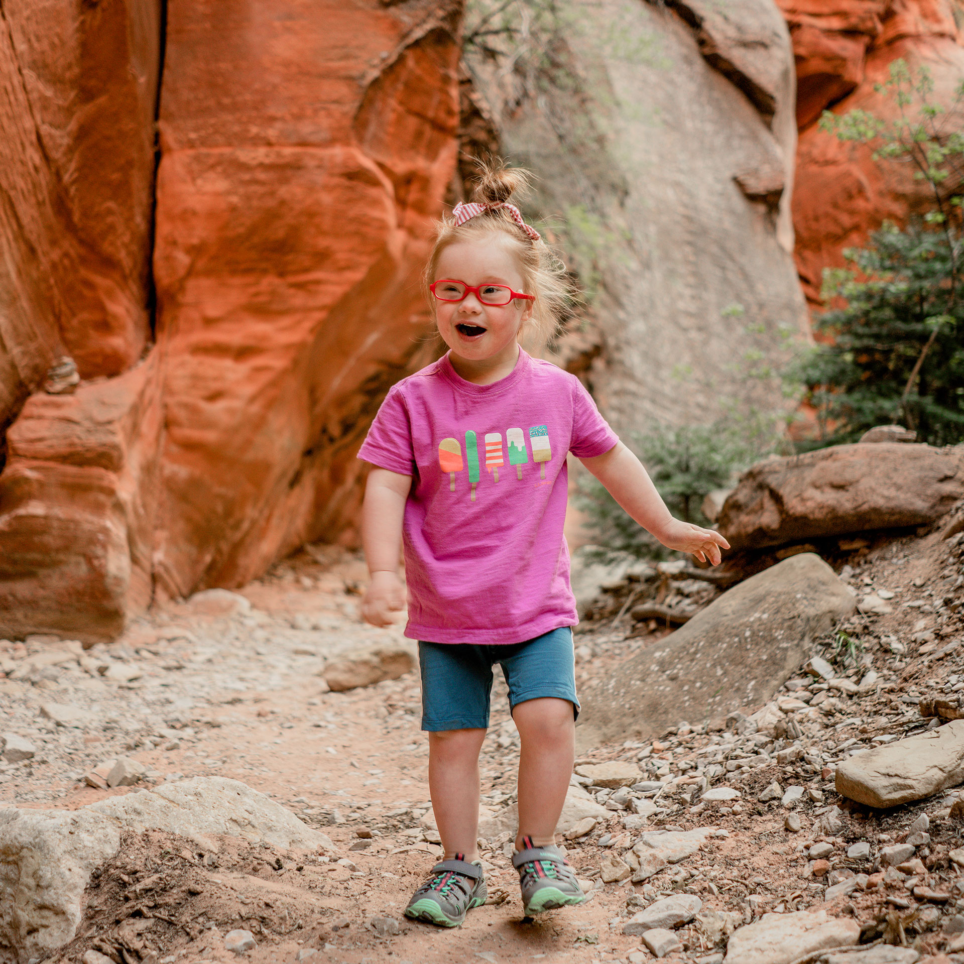 Featured Contributor, Melody Forsyth's daughter, Ruby walks in front of a rock formation in a pink t-shirt and shorts.