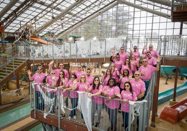 A group of volunteers standing in an indoor water park facility and waving at the camera.