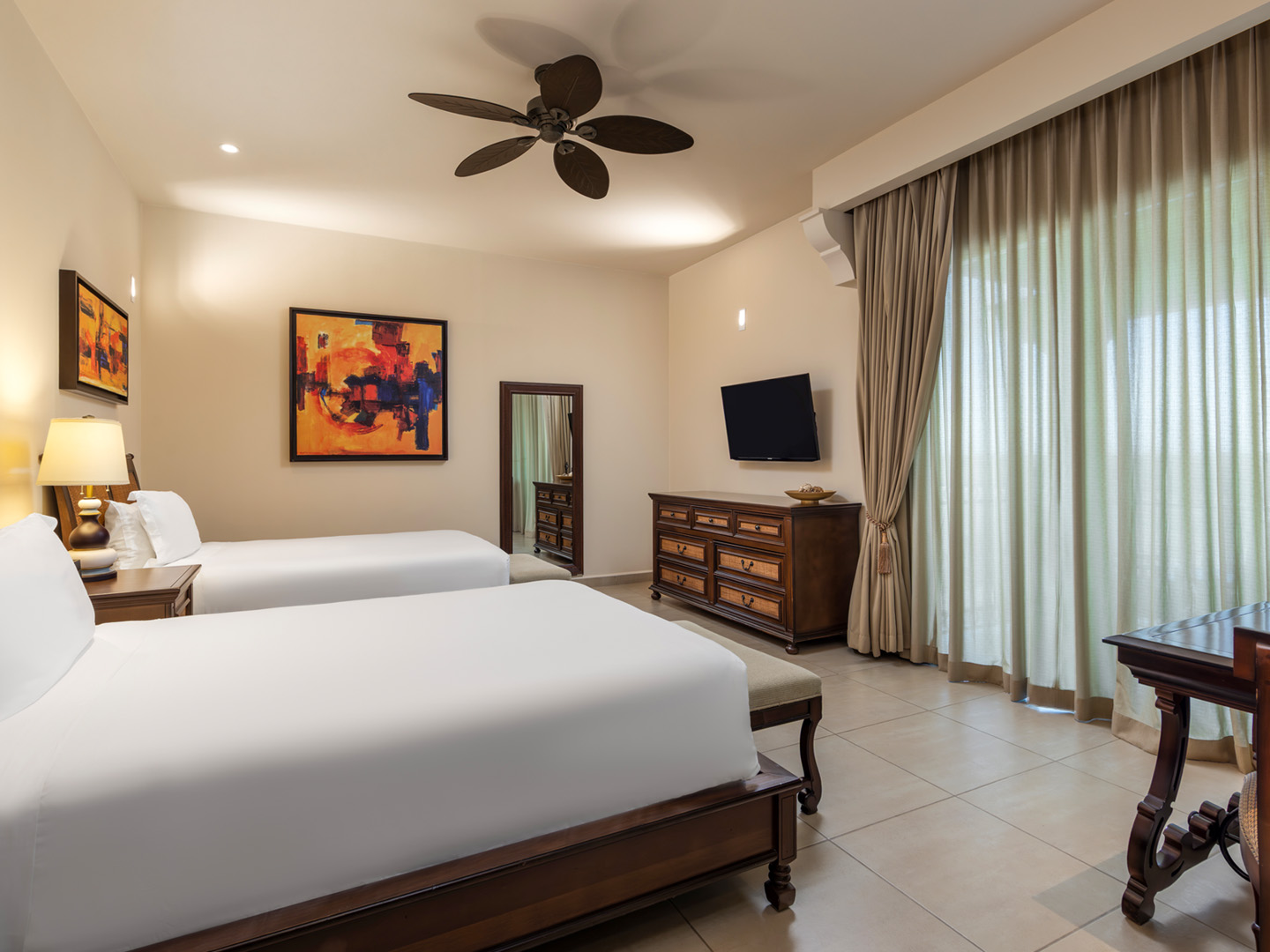 Suite bedroom with double beds, dresser, TV, and large window. 