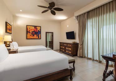 Suite bedroom with double beds, dresser, TV, and large window.