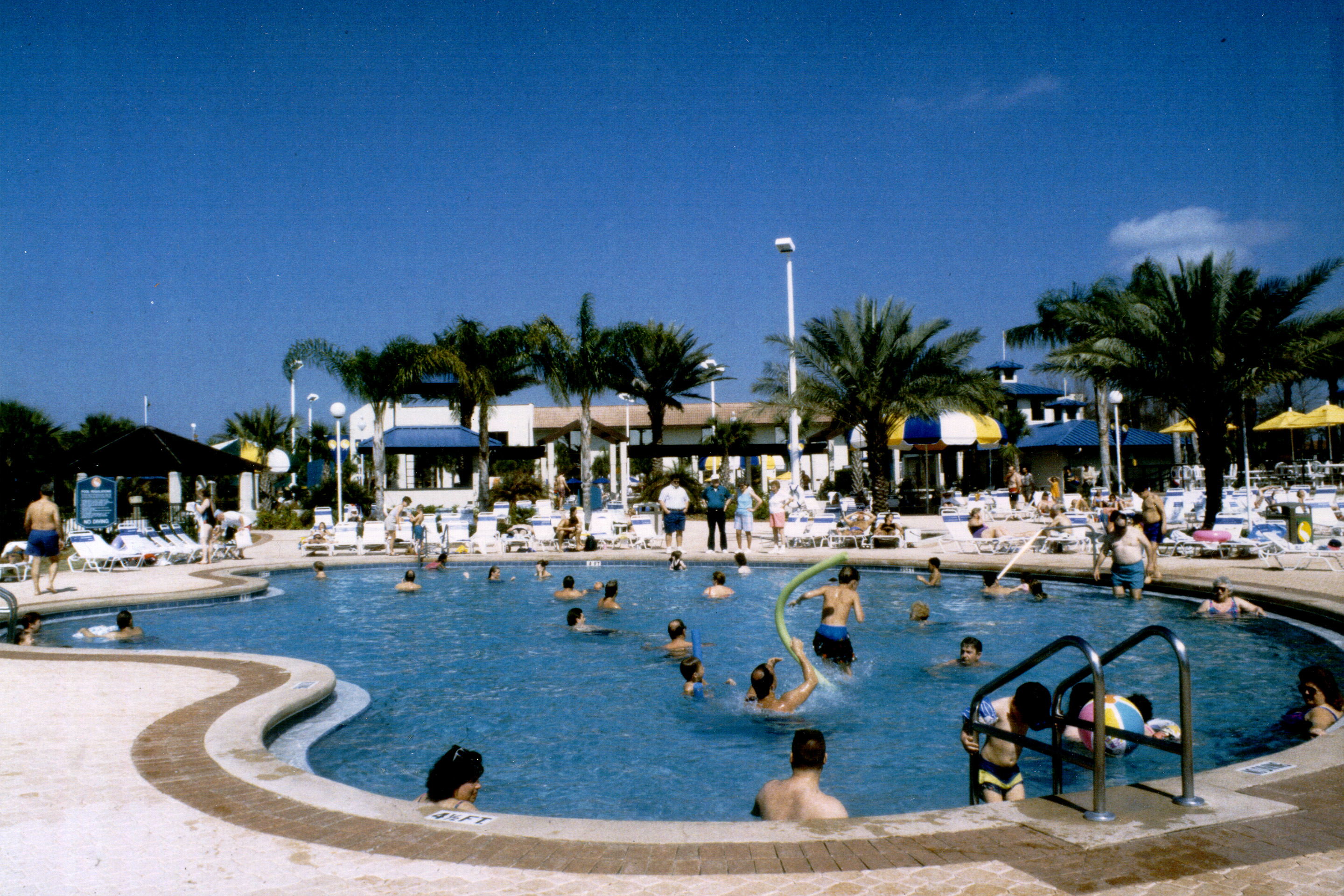 An old photograph of guests swimming in an outdoor pool under a blue sky