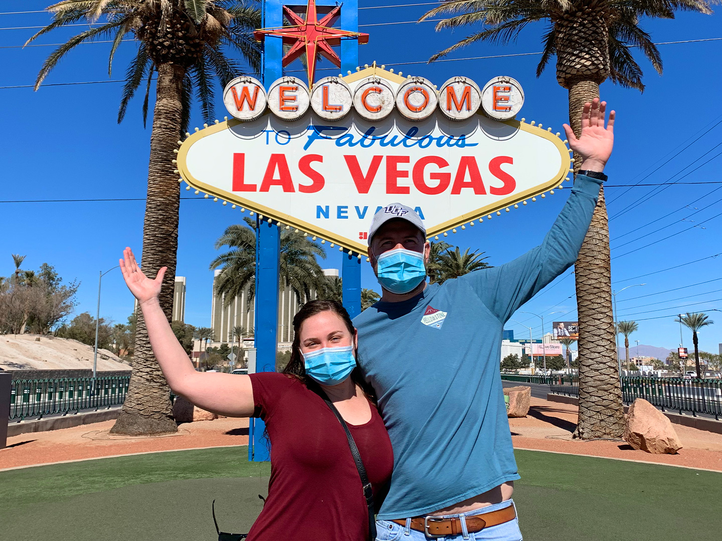 Featured Contributor, Ashley Fraboni (left) and her fiancé, Nicholas (right), pose in front of the 'Welcome to Las Vegas' marquee while wearing face masks.