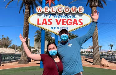 Featured Contributor, Ashley Fraboni (left) and her fiancé, Nicholas (right), pose in front of the 'Welcome to Las Vegas' marquee while wearing face masks.