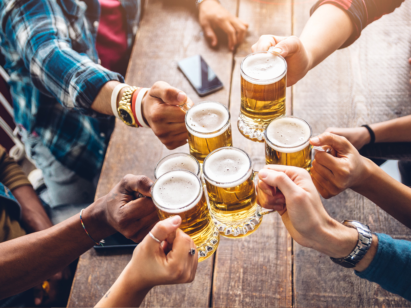 Several people hold their glasses of beer over a table giving 'cheers' to each other.