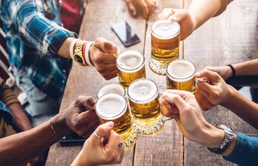 Several people hold their glasses of beer over a table giving 'cheers' to each other.