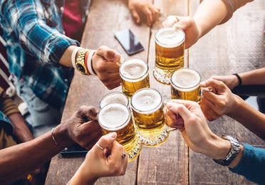 Several people hold their glasses of beer over a table giving 'cheers' to each other.