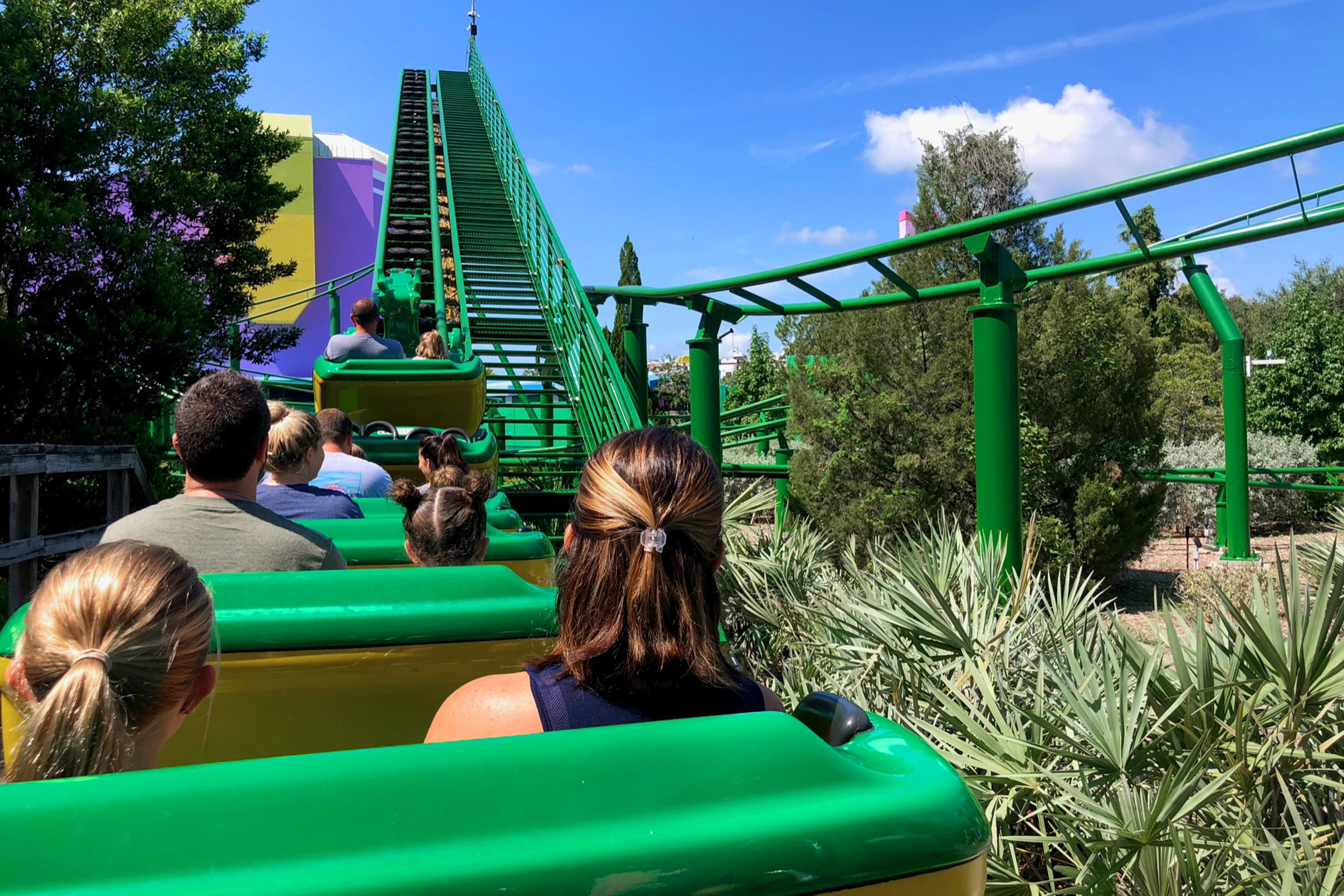 A young girl (left) and woman (right) sit several rows behind guests on a green outdoor rollercoaster.