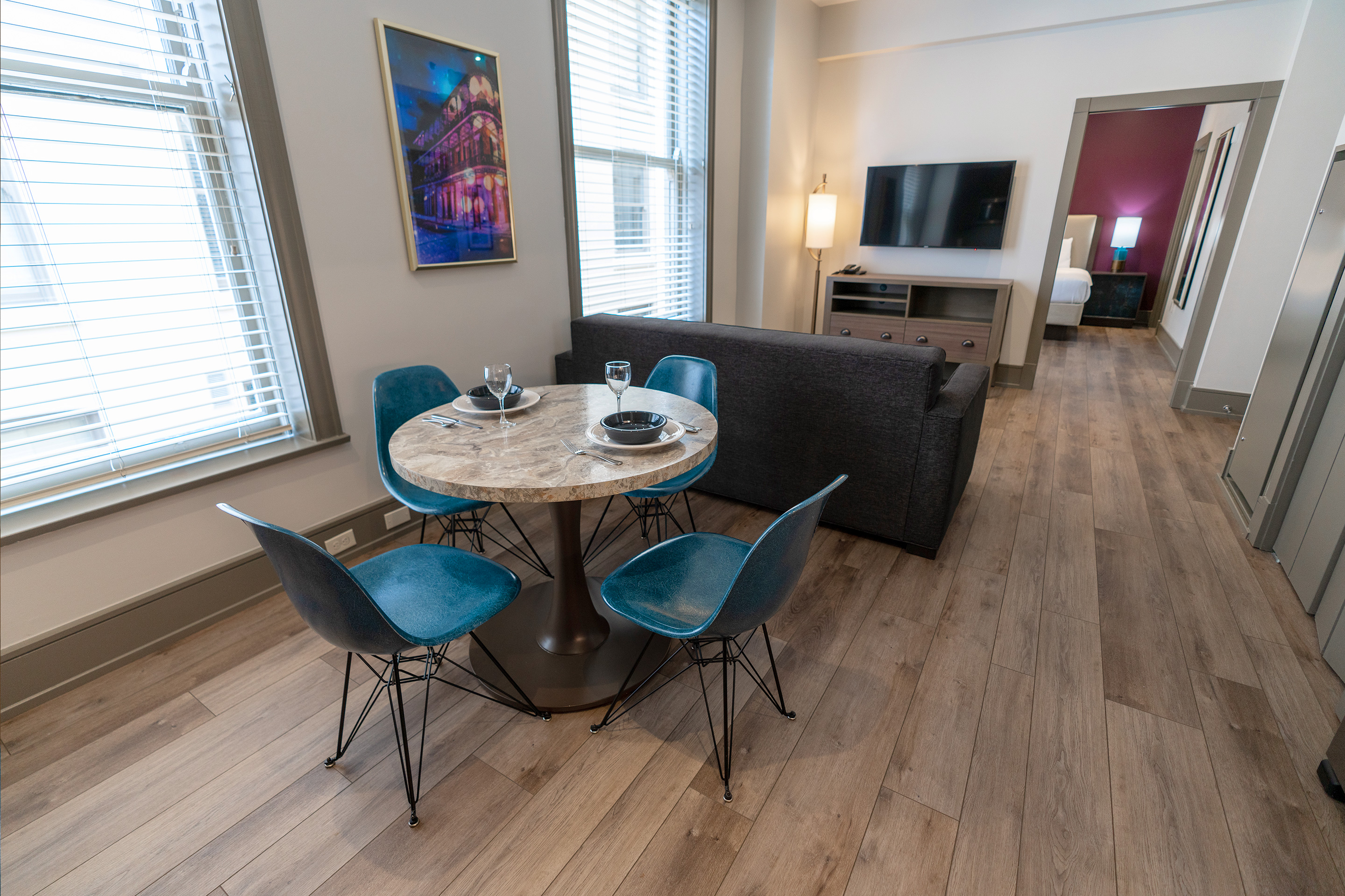 The interior of our one-bedroom standard villa at our New Orleans resort furnished with a round marble-top dining table with four chair and two place settings near a grey couch with a tv unit and a bedroom in the distance.