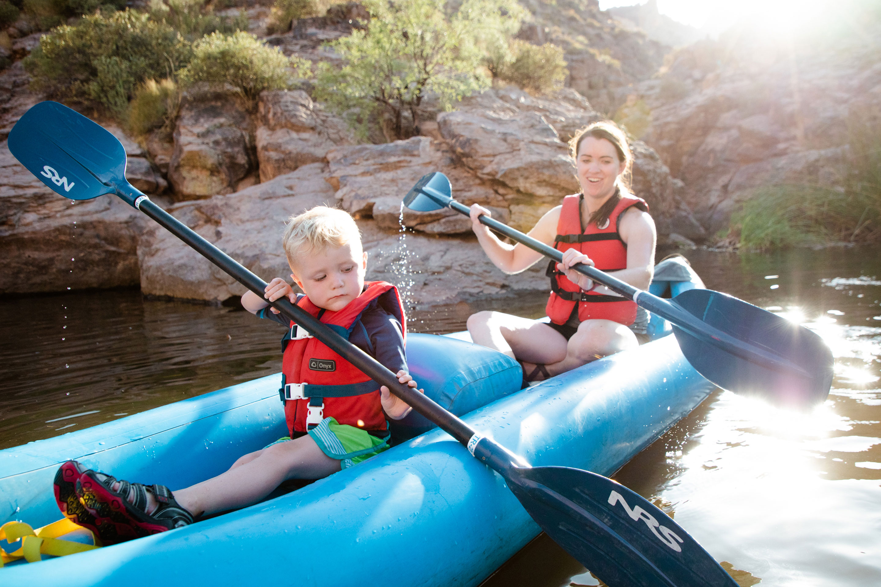 Author Jessica Averett (right) and her son (left) wear life jackets as they paddle their kayak in the water.