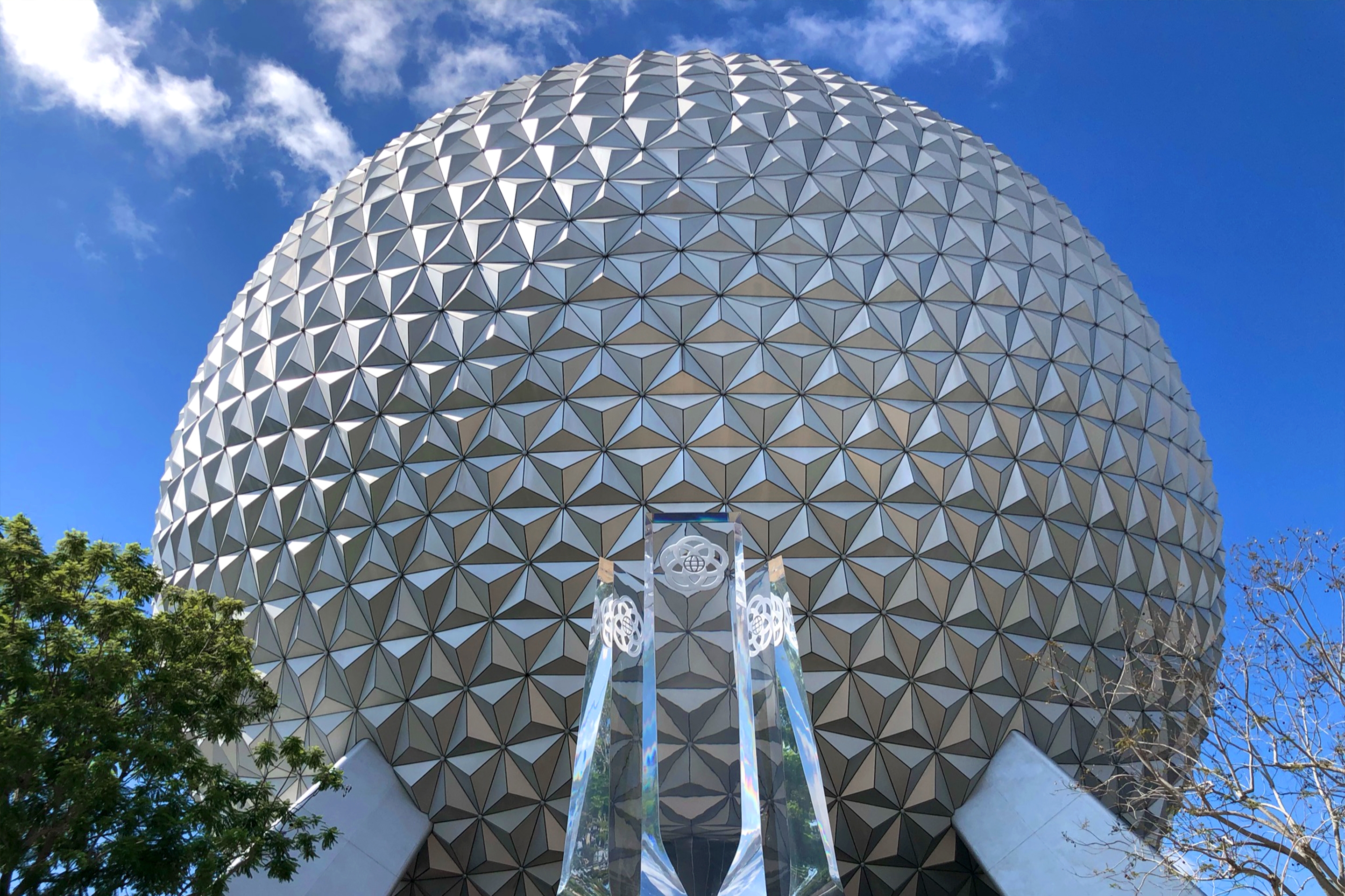 The Geosphere that holds Spaceship Earth at Epcot stands under a blue sky with new acrylic pylons representing the past, present and future of Epcot.