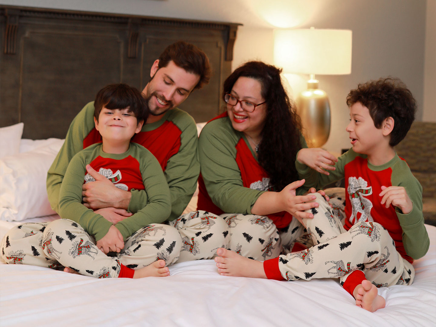 Two young boys, a man and woman wear matching pajamas on a bed.