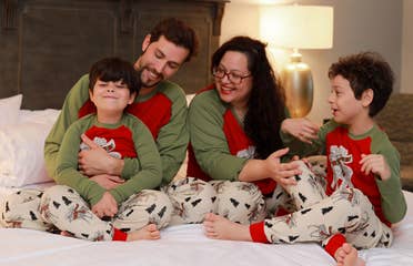 Two young boys, a man and woman wear matching pajamas on a bed.