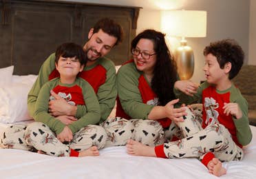 Two young boys, a man and woman wear matching pajamas on a bed.