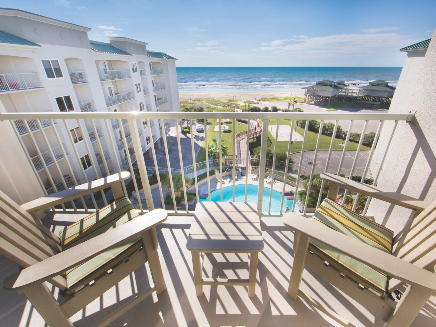 2 adirondack chairs sit on balcony overlooking pool and ocean.