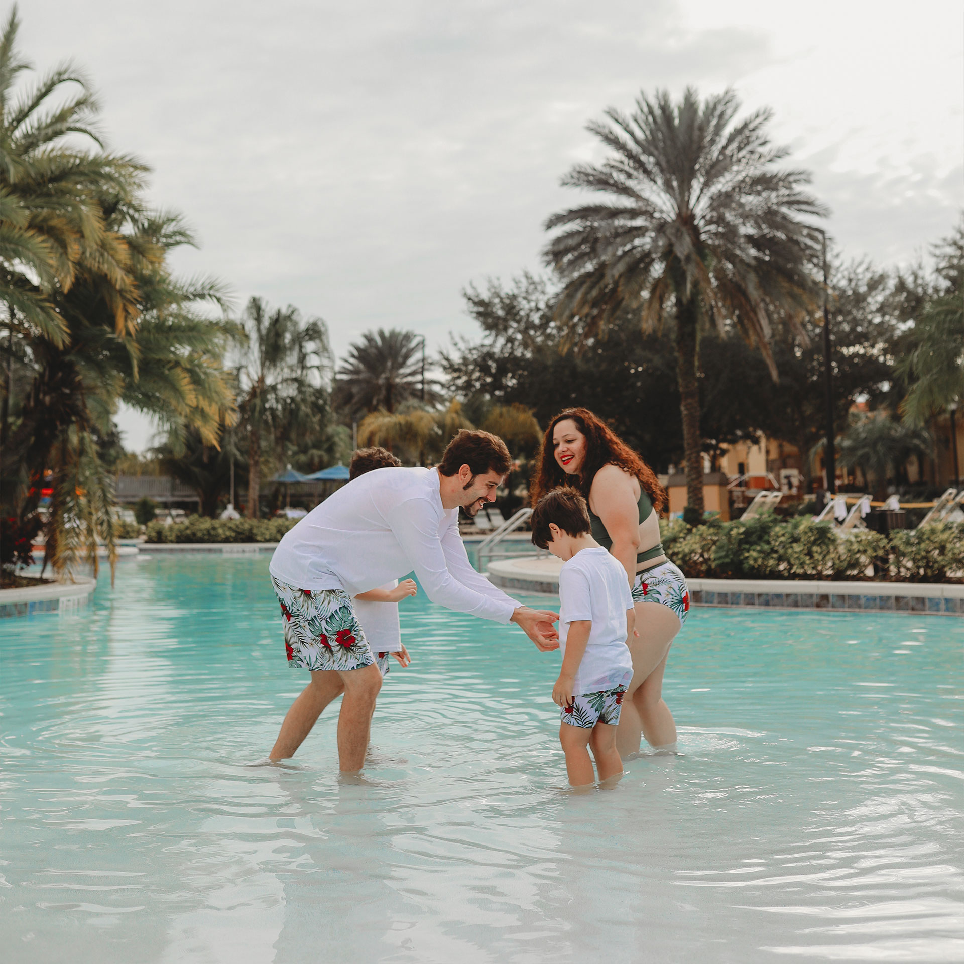 A woman, man and two young boys wear swimwear while standing in a zero-entry pool outdoors.