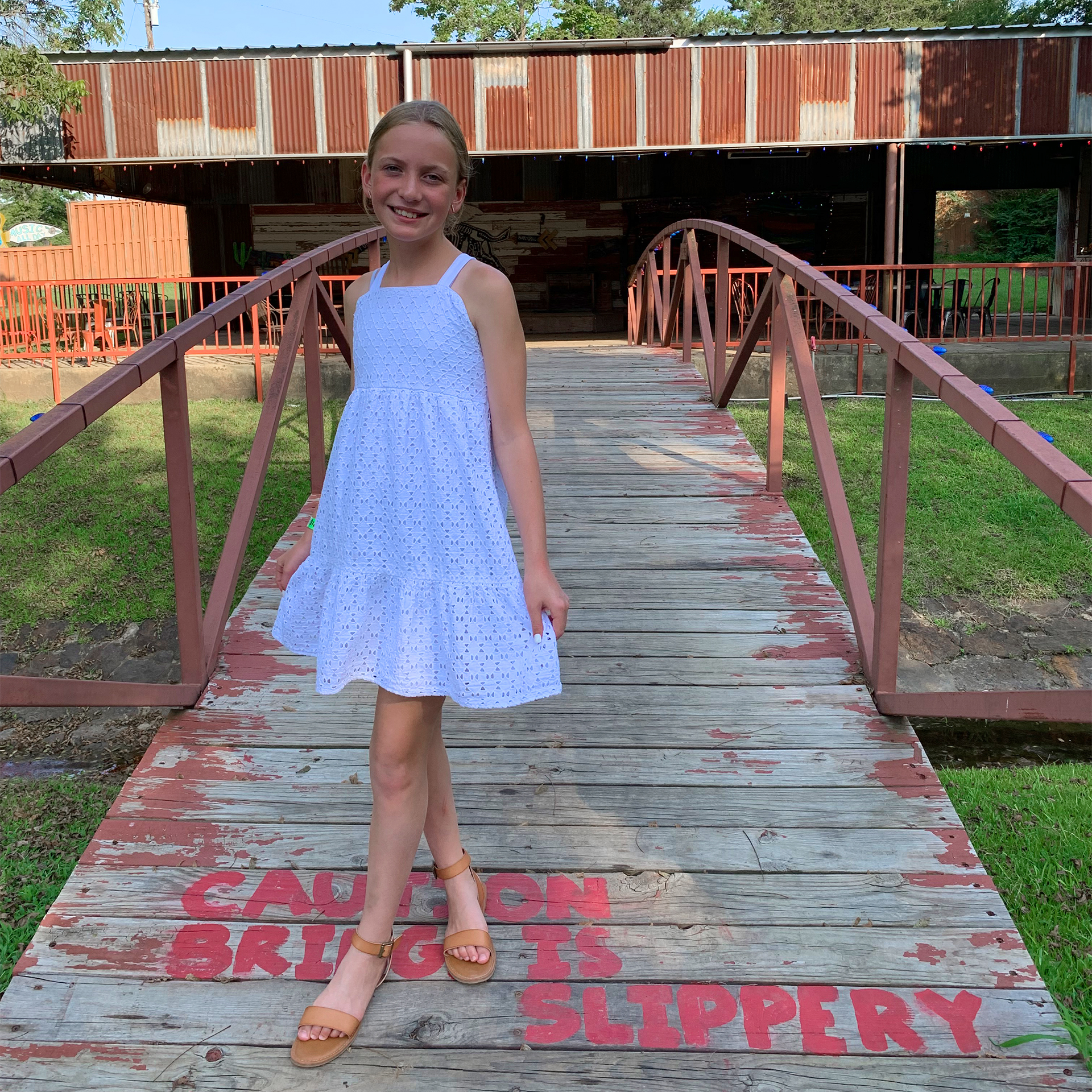 A caucasian girl wears a white dress near a bridge.