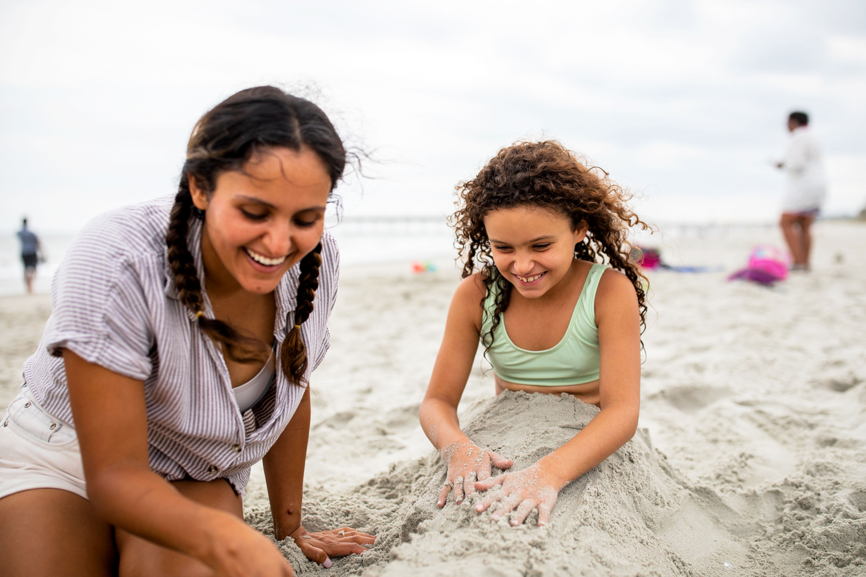 Brenda and her daughter play on the beach by burying Victoria in sand.