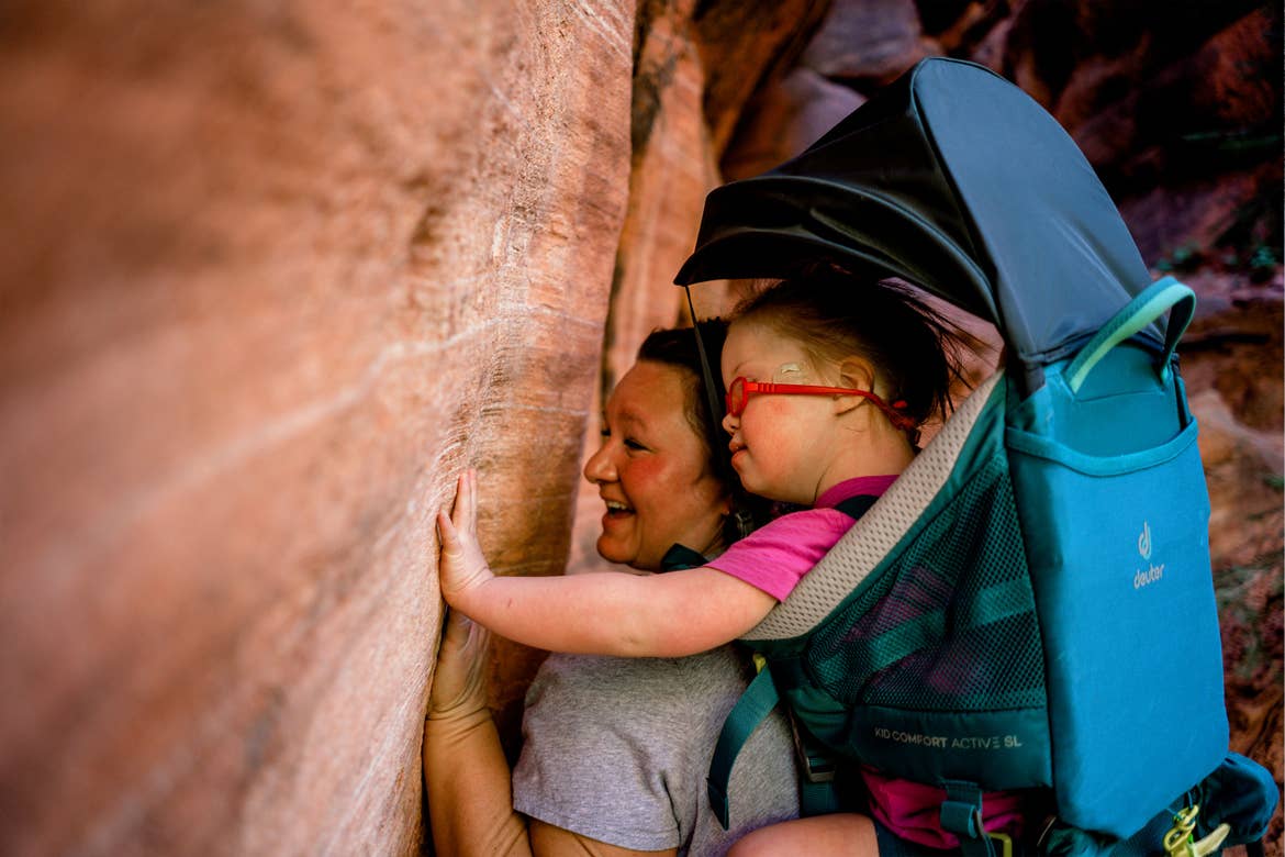 Featured Contributor, Melody Forsyth (left), backpacks with her daughter, Ruby (right), as they touch some rock formations.