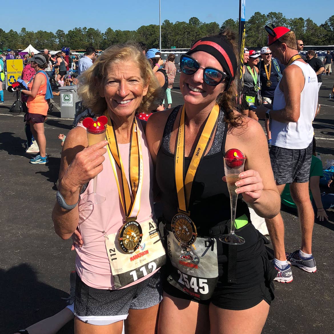 Co-author, Christine (right), wears a medal, black tank top and shorts while holding a Mickey drink with her mom (left).