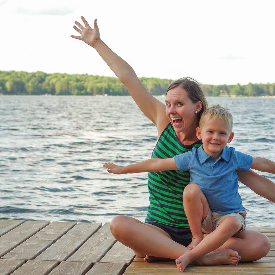 Author, Sarah Conroy, and son, Logan, sit on a lake pier mimicking an airplane with their arms.