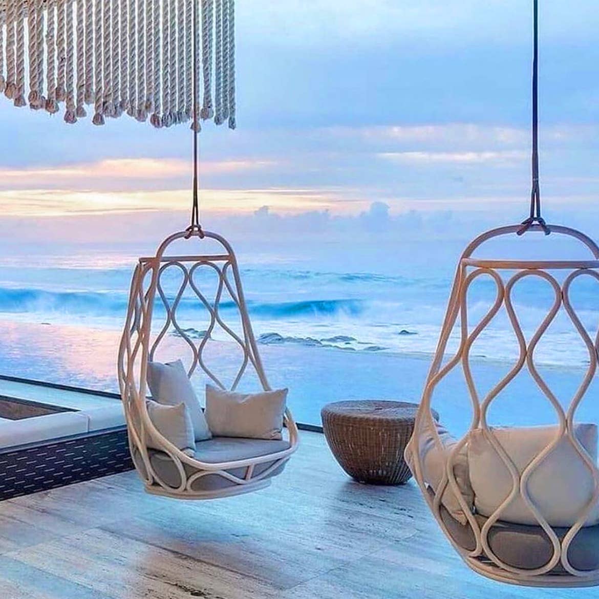 Two hanging, swing chairs overlook the ocean on a tiled patio outdoors.