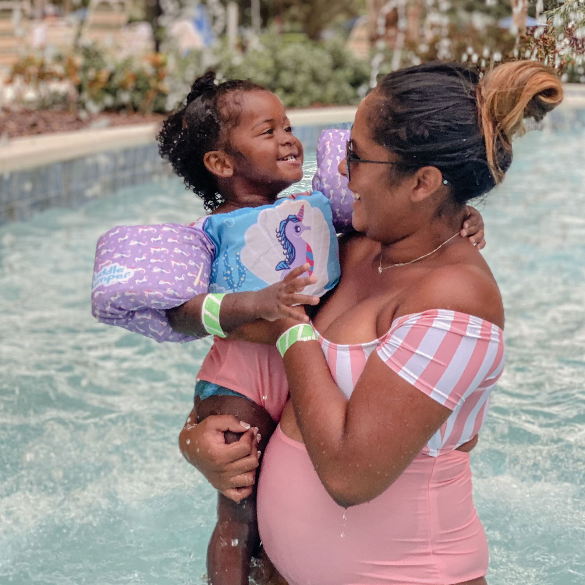 Author, Kimberly Gelin (right), poses in a striped pink swimsuit as her daughter, wears her swimsuit and floaties in our pool at Orange Lake Resort in Florida.