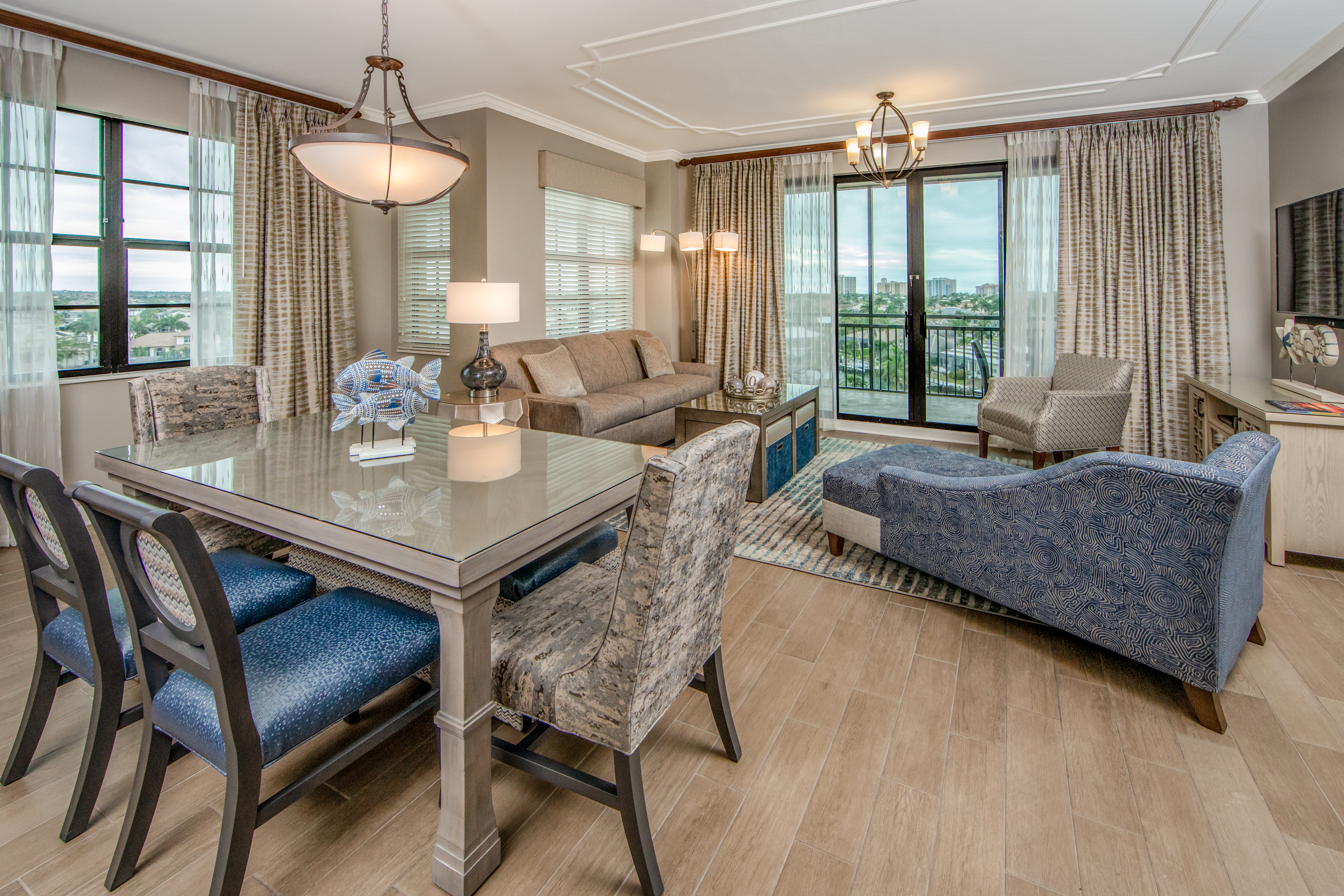 View of dining room table with six chairs, full living room, and access to furnished balcony in a three-bedroom villa at Sunset Cove Resort in Marco Island, Florida