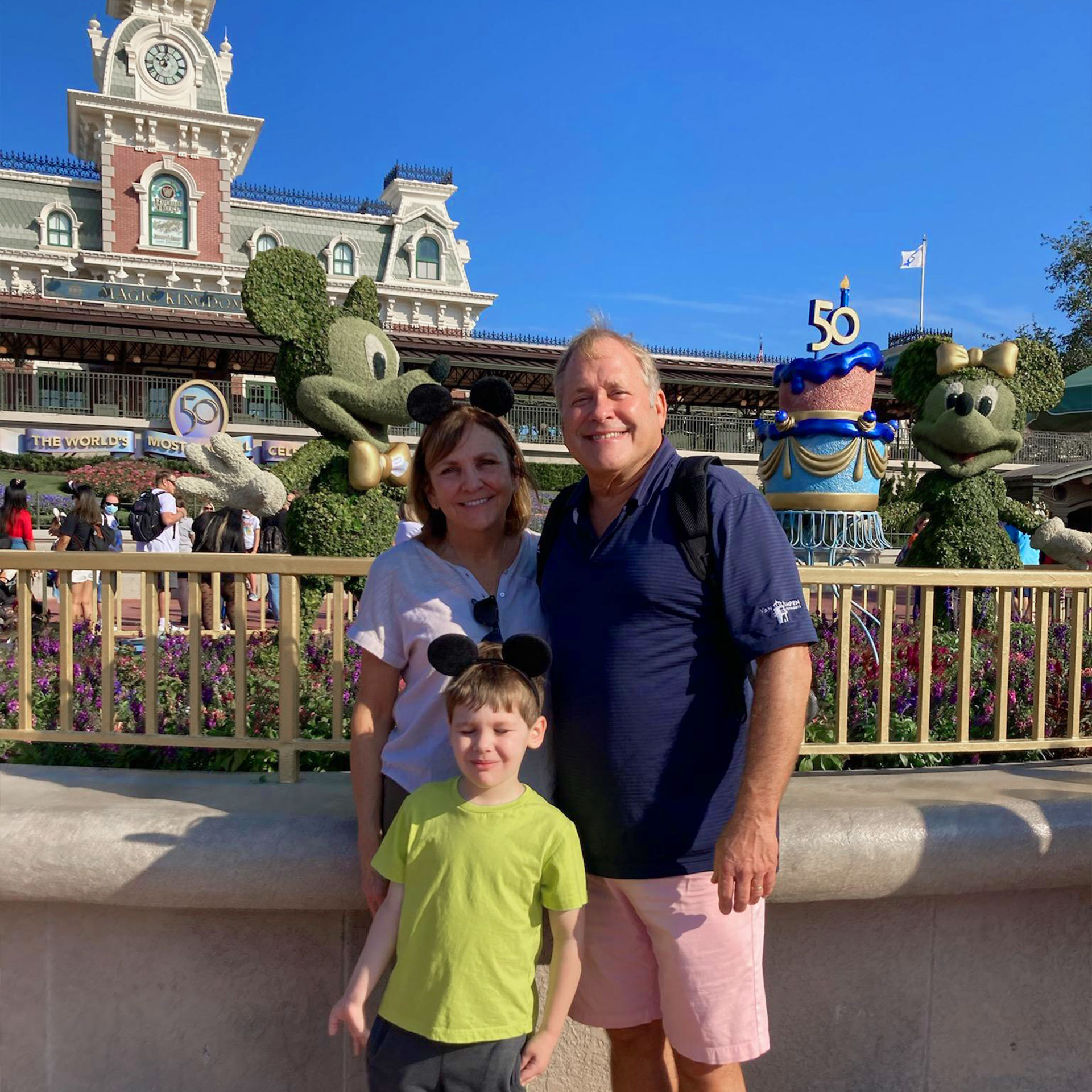 A woman, man and young boy wearing mouse ears stand in front of a pair of topiaries at Walt Disney World.