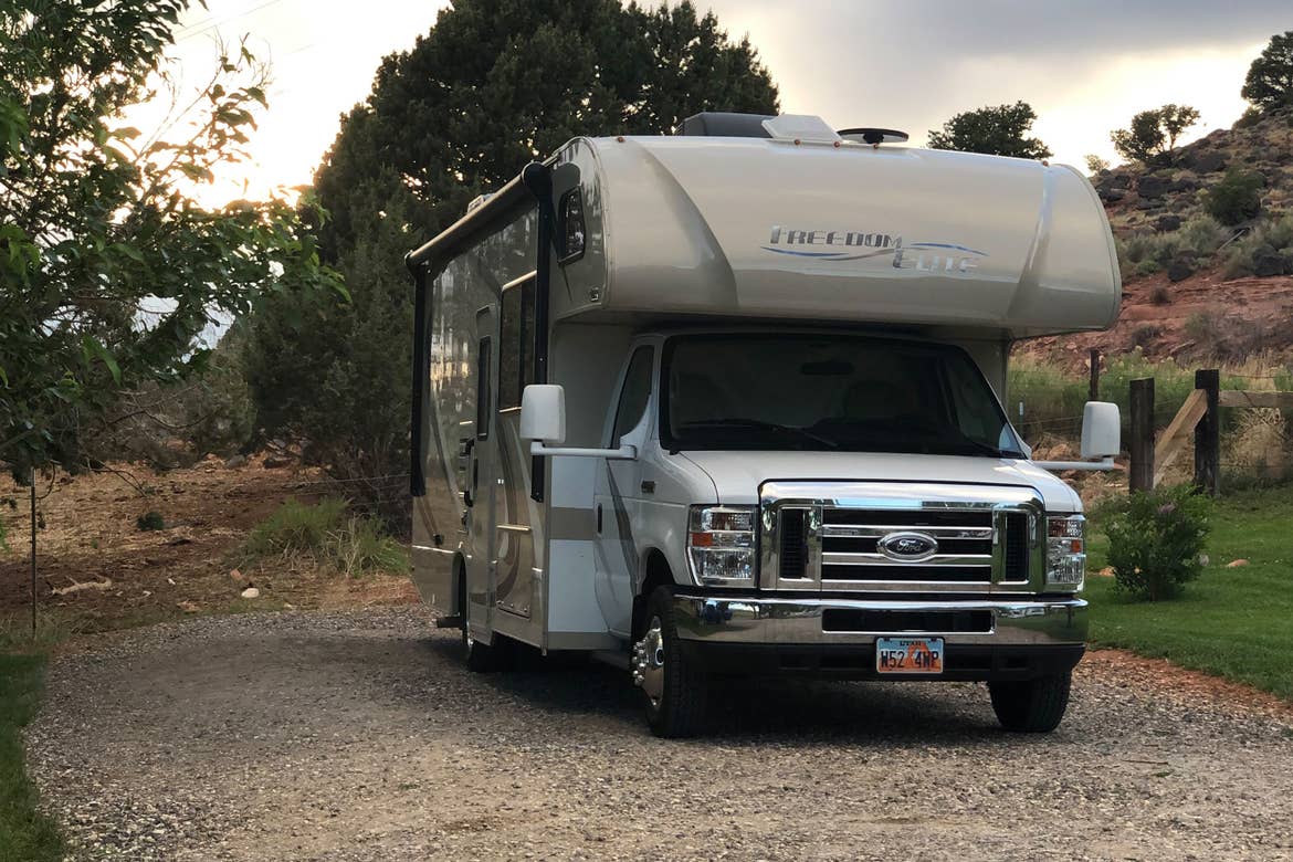 Chris' RV rental sitting in an RV parking lot with Utah red rocks and greenery in the distance.