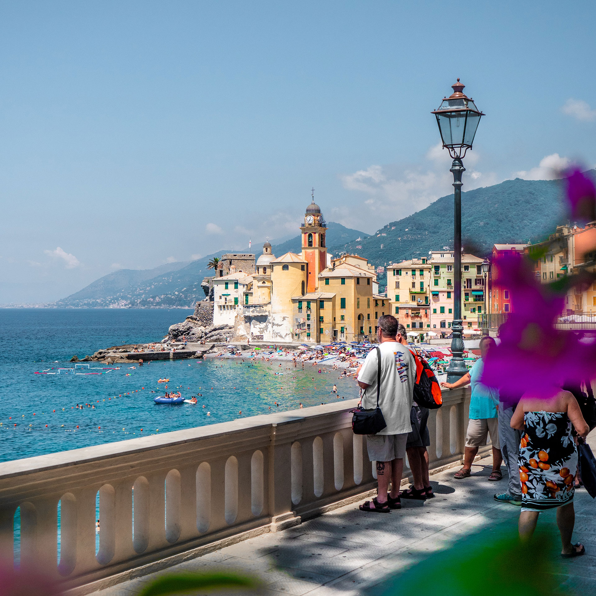 A group of guests (right) stand on a bridge looking out to the ocean as the city of Capri can be seen in the background.