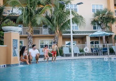 Family of four sitting on edge of pool at Cape Canaveral Beach Resort in Florida.