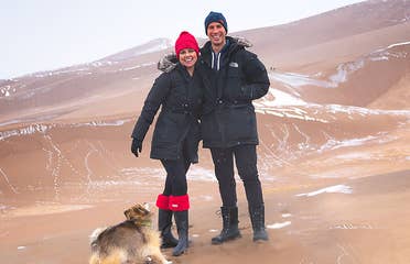 Authors, Lauren Layne and Anthony LeDonne, stand in winter apparel with Bailey the Pomeranian at the Great Sand Dunes National Park and Preserve.
