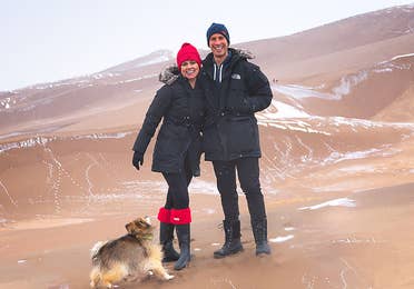 Authors, Lauren Layne and Anthony LeDonne, stand in winter apparel with Bailey the Pomeranian at the Great Sand Dunes National Park and Preserve.