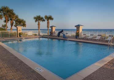 Outdoor pool surrounded by palm trees with beachfront view at Panama City Beach Resort in Florida.