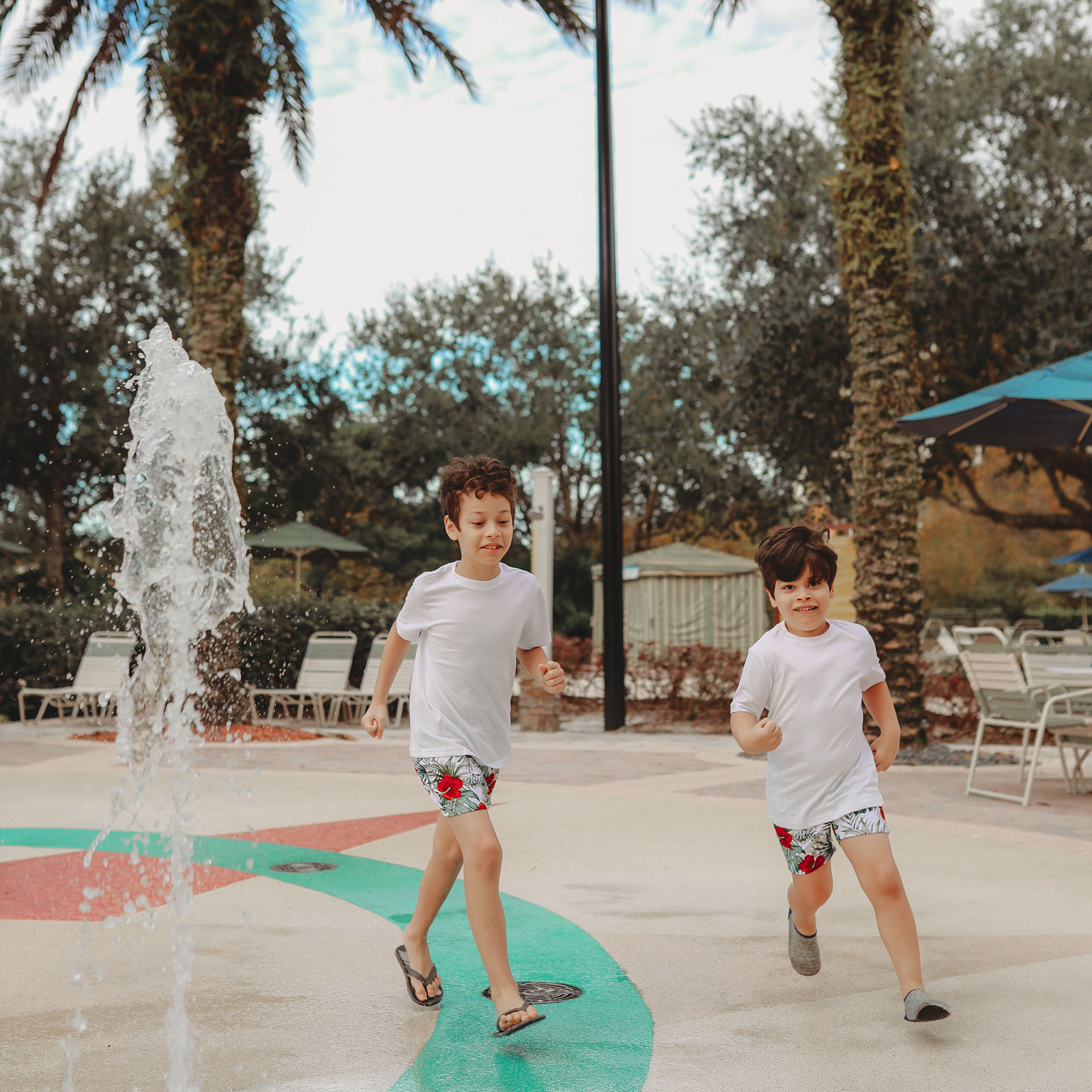 Two young boys in swimwear run though an outdoor splash pad.