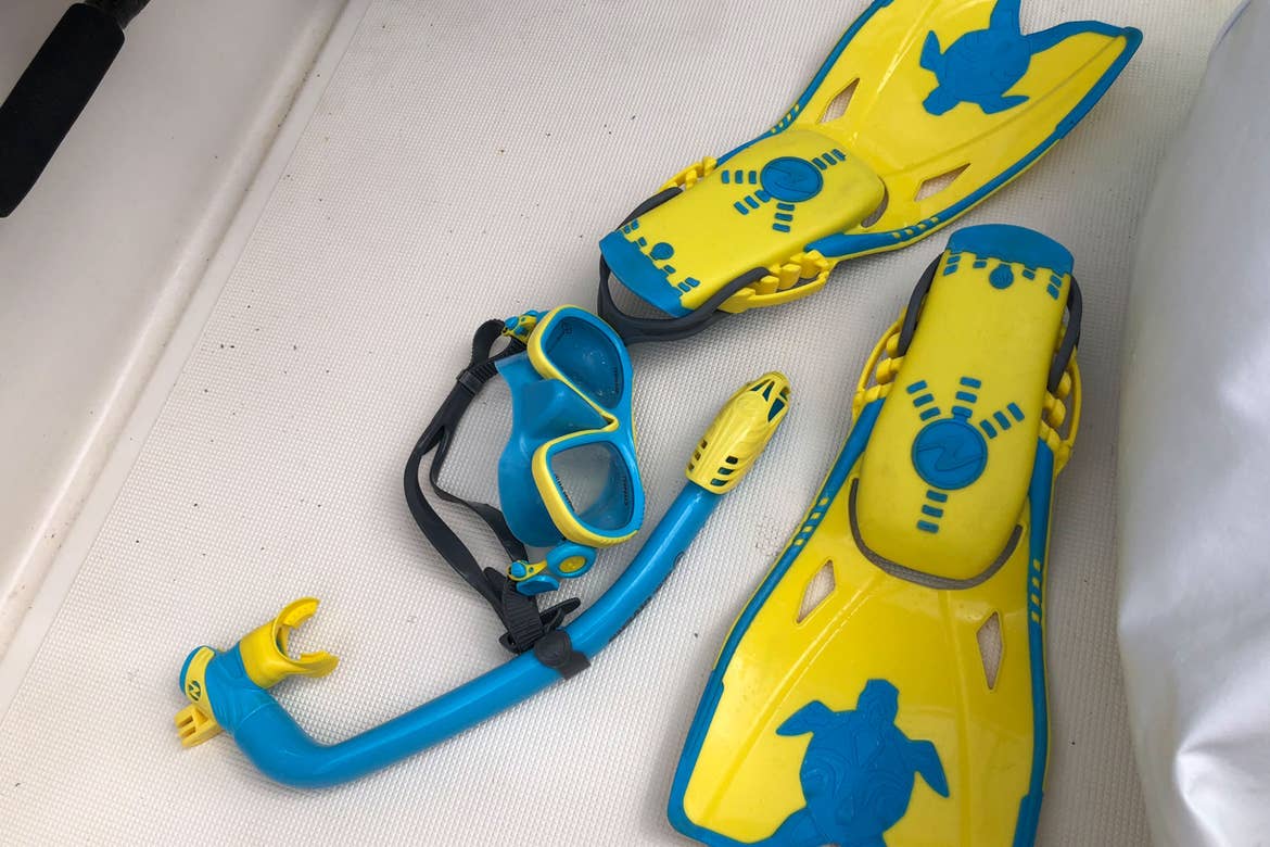 A pair of yellow and blue swimming fins and matching snorkel gear placed on the floor of a boat.