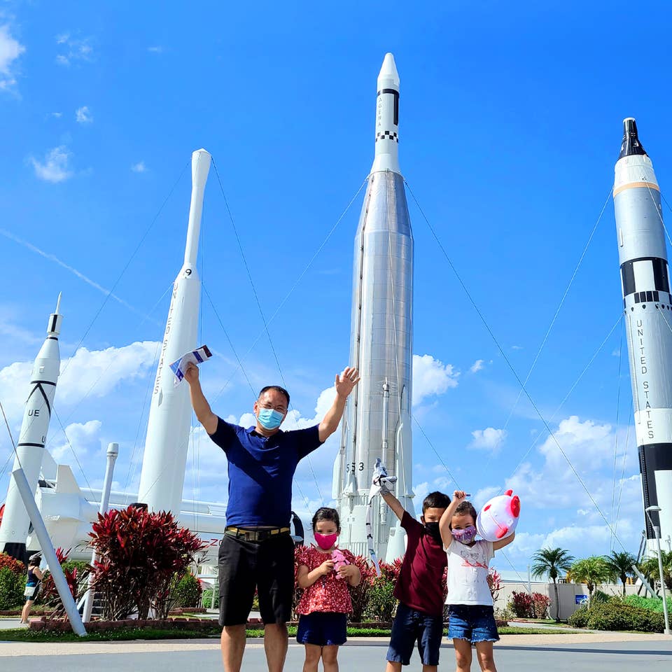 Featured Contributor, Angelica Kajiwara's husband and three children run pose in front of a 'Rocket Playground' located at the Kennedy Space Center™ Visitor Complex.