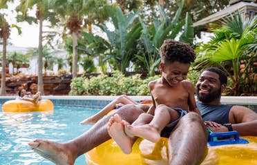 A young boy and his father sit on an orange inner tube in the lazy river in River Island at our Orange Lake resort located in Orlando, FL.