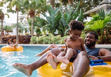 A young boy and his father sit on an orange inner tube in the lazy river in River Island at our Orange Lake resort located in Orlando, FL.