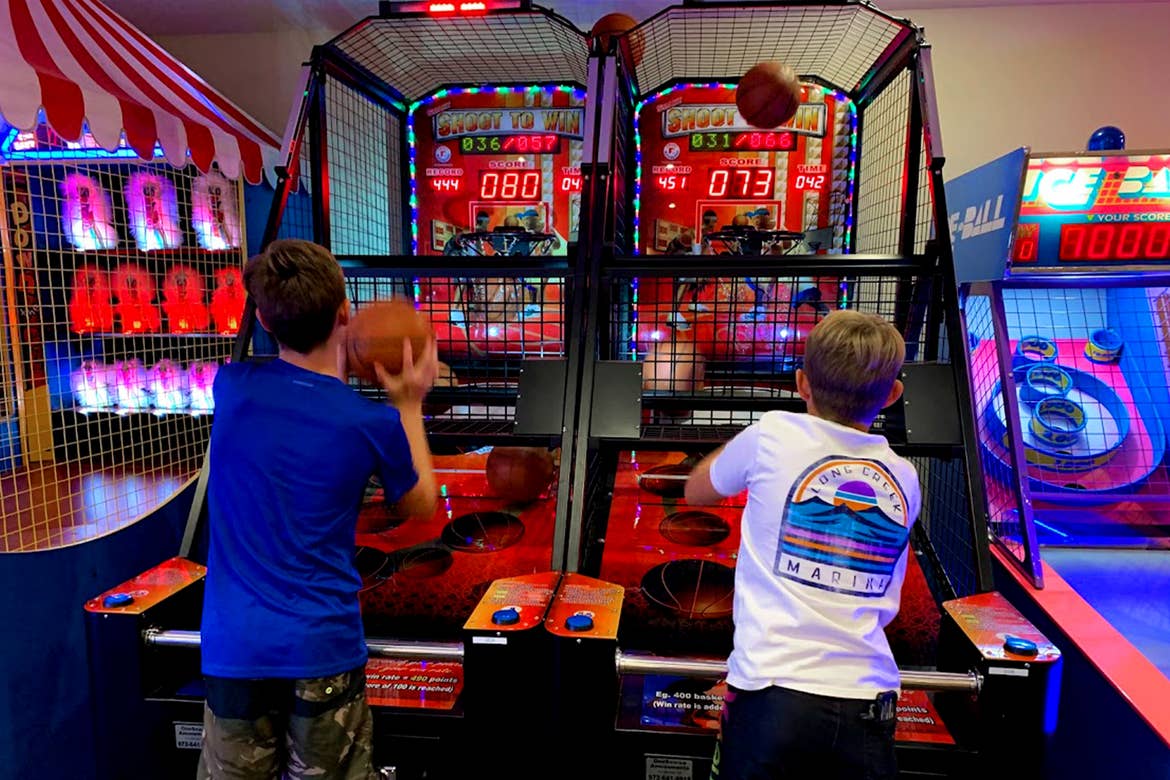 Two boys play a basketball arcade game.